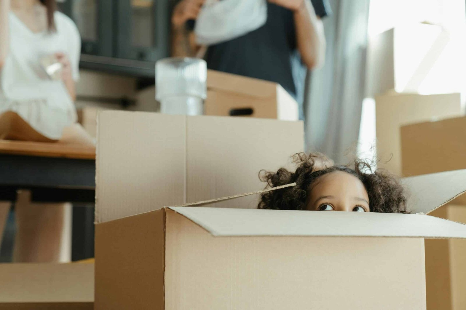 A child peeks out of a cardboard box while moving into a new home, capturing a playful moment.